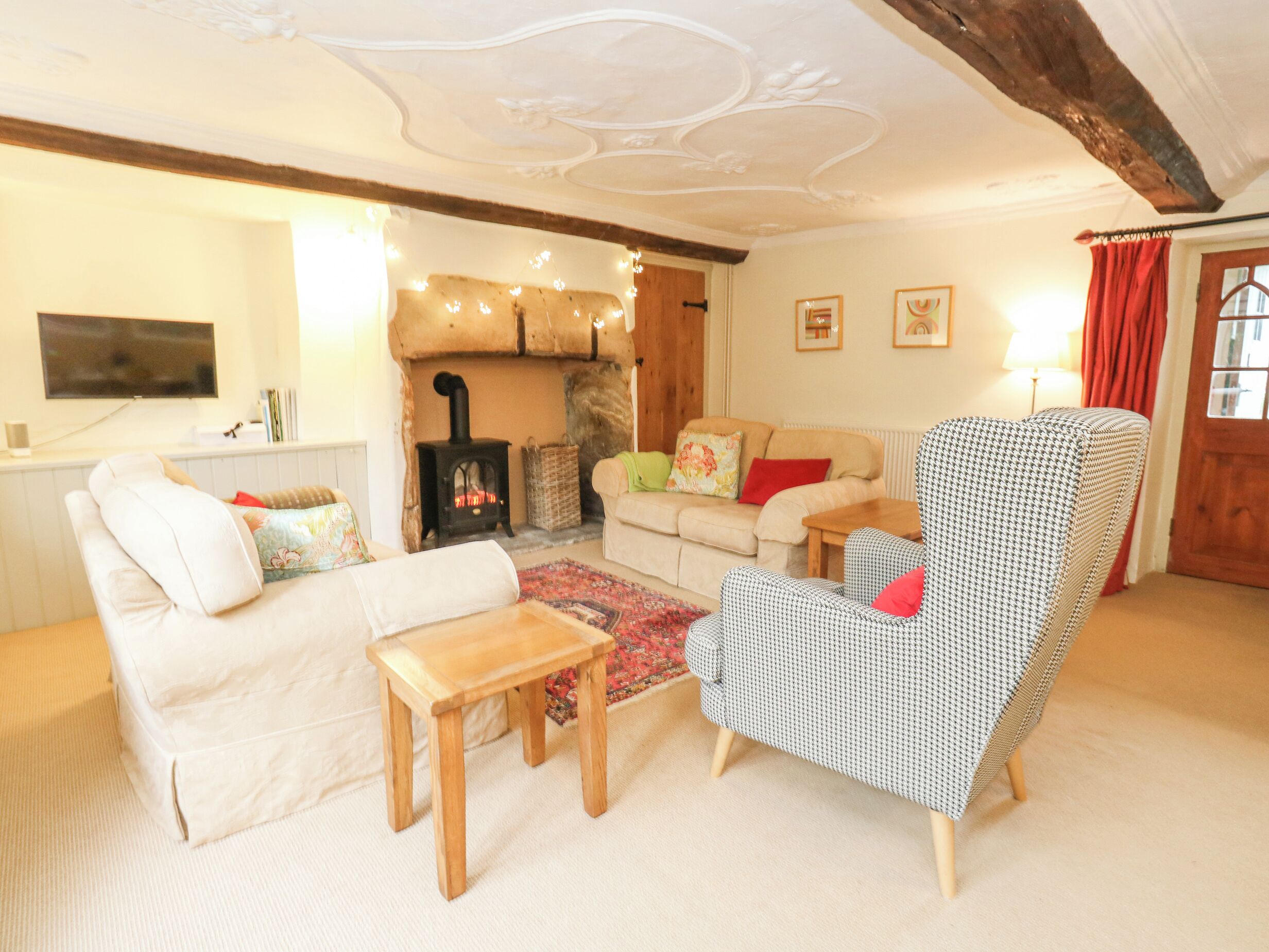 A cozy living room with a sofa, armchair, and a small wooden table. A fireplace is visible in the background, and a television is mounted on the wall.