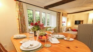 A dining table set with plates, glasses, and a fruit bowl, in a room with a sofa and a television. - The Elbow (Dorchester)