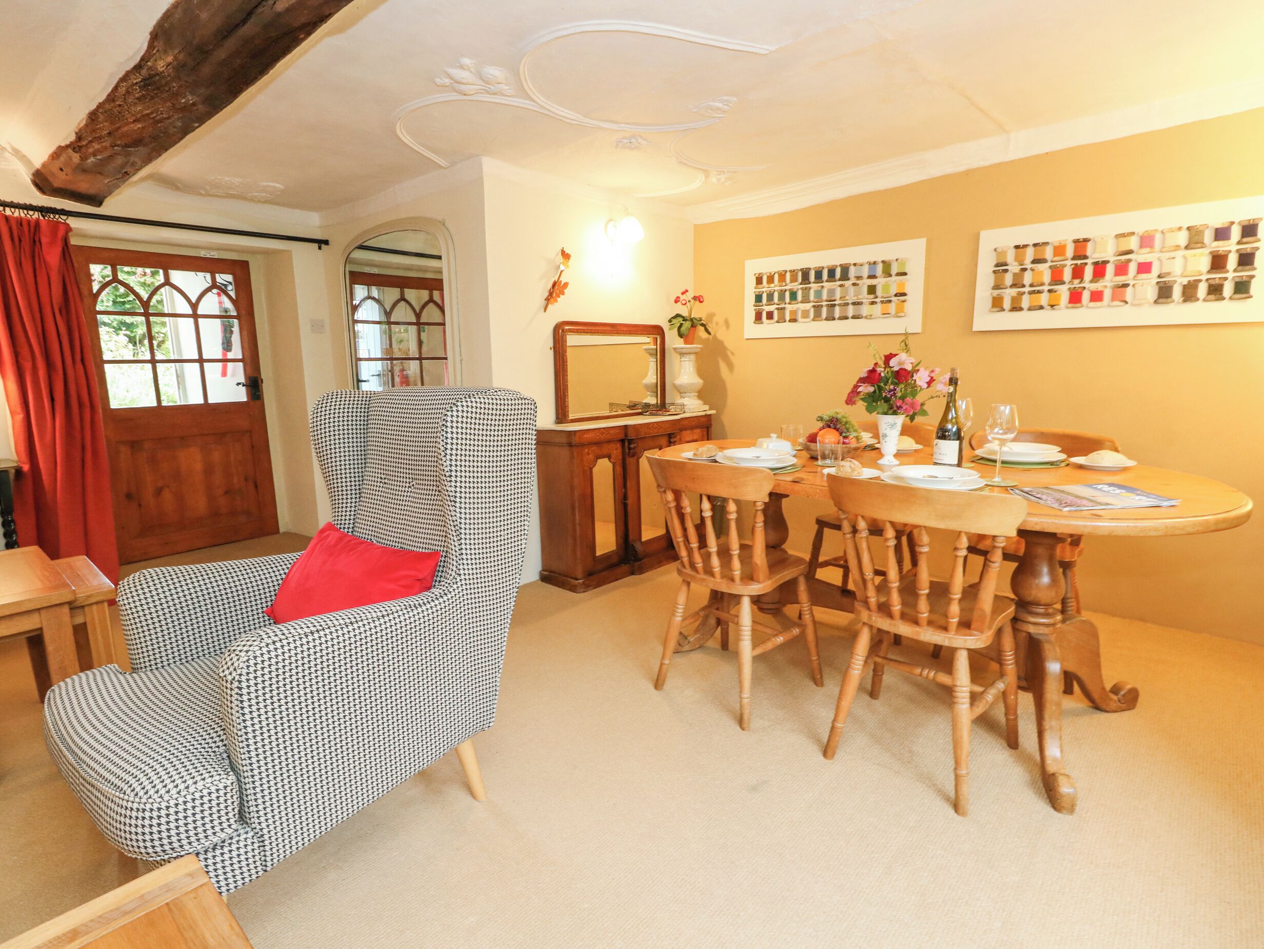 A dining area with a wooden table, chairs, and a houndstooth patterned armchair with a red pillow.