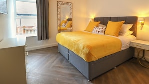 Quarto com uma cama grande, mesa de cabeceira, espelho e janela com cortinas.
