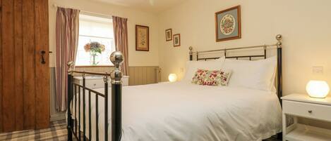 A bedroom with a bed, a bedside table, a nightstand, a window with curtains, a chandelier, and a door.