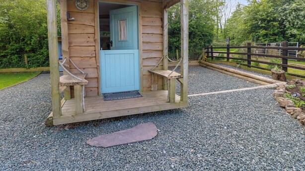 A wooden cabin with a blue door, a small porch, and a gravel path leading to it. - Llety Llanfair (Caernarfon)