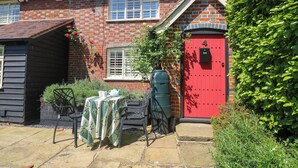 Ein Backsteinhaus mit roter Tür, ein kleiner Garten mit Tisch und Stühlen sowie ein grüner Wassertank.