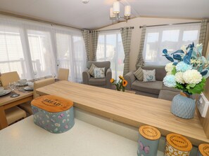 A cozy living area with a wooden coffee table, a sofa, and a dining table set for two. There are decorative vases with flowers and a small stool. - The Beachhouse (Chichester)