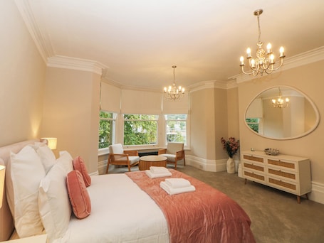 A bedroom with a large bed, a desk, and a chair, a dresser, and a large mirror.