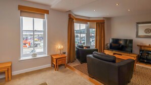 A modern living room with a large window, a flat-screen TV, a sofa, and a small wooden table. - 43A Quay Street (Scarborough)
