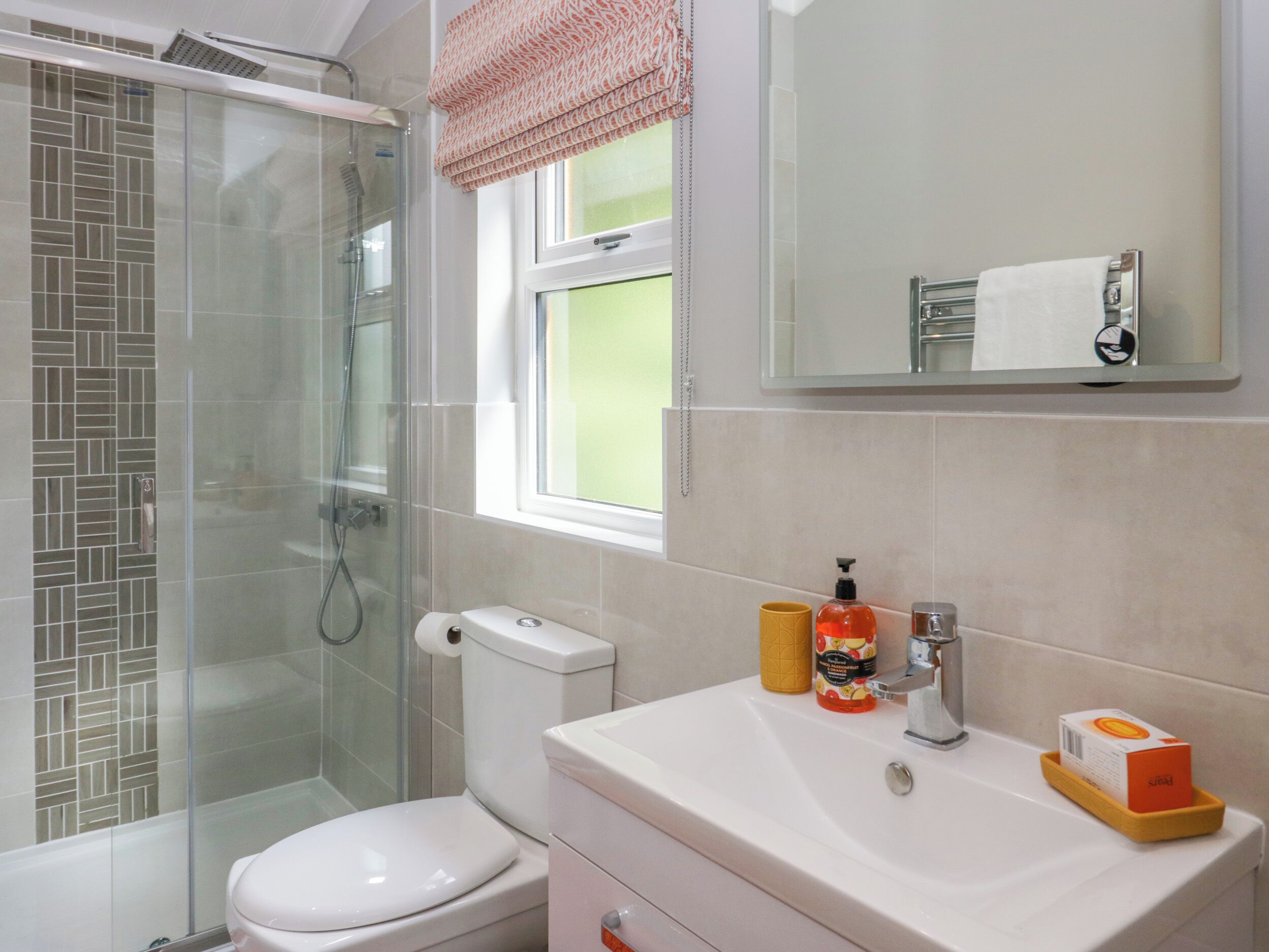 Ein Badezimmer mit Duschkabine aus Glas, Toilette, Waschbecken mit Pflegeprodukten und Spiegel über dem Waschbecken.