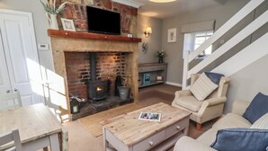 A living room with a brick fireplace, a television mounted above it, a sofa, a coffee table, and a staircase in the background. - Aln Cottage (Alnwick)