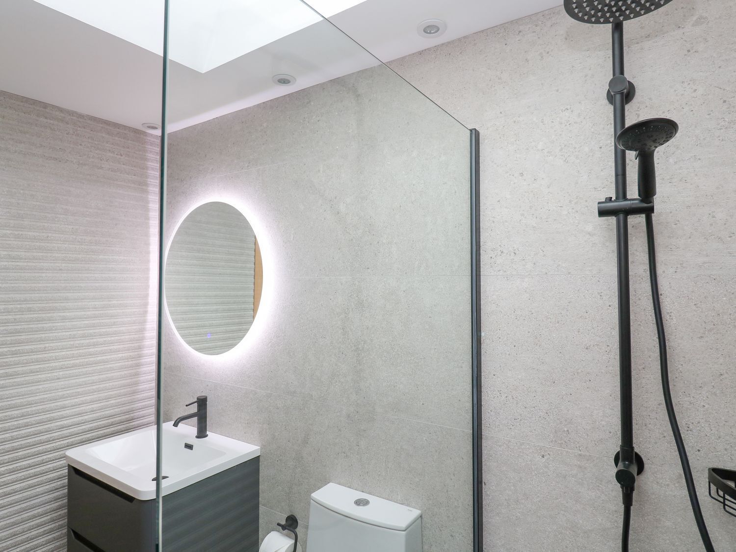 A modern bathroom with a glass-enclosed shower, a round mirror, and a white sink.