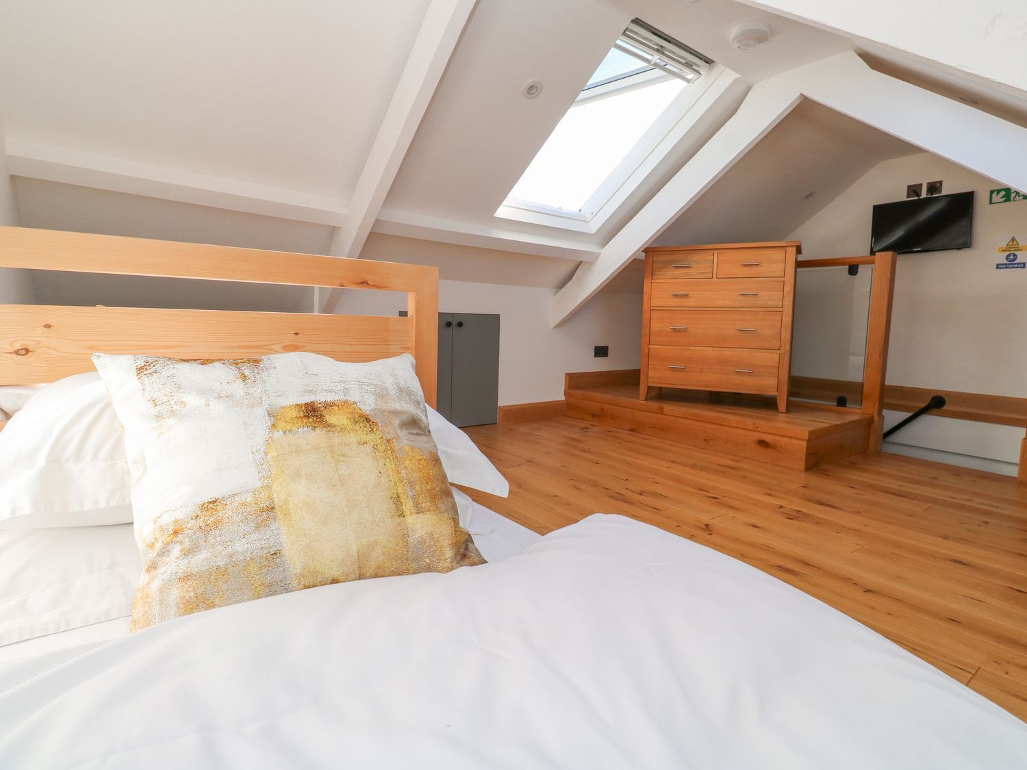 A bedroom with a sloped ceiling, wooden furniture, a bed with white bedding, and a television on the wall.