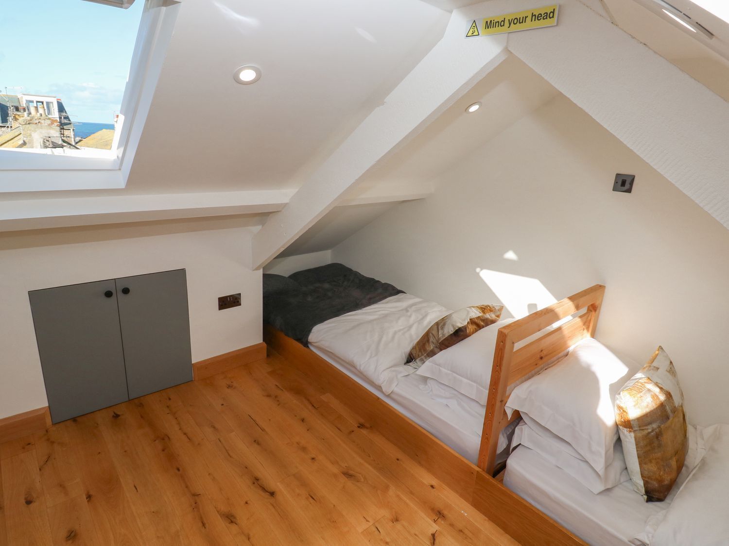 Una camera da letto piccola con tetto spiovente, un lucernario, un letto, un armadio in legno e vista sul mare.