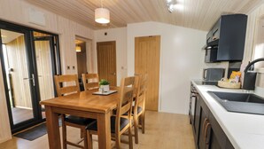 A compact kitchen with a wooden dining table, chairs, and a white countertop. - Betsi (Ruthin)