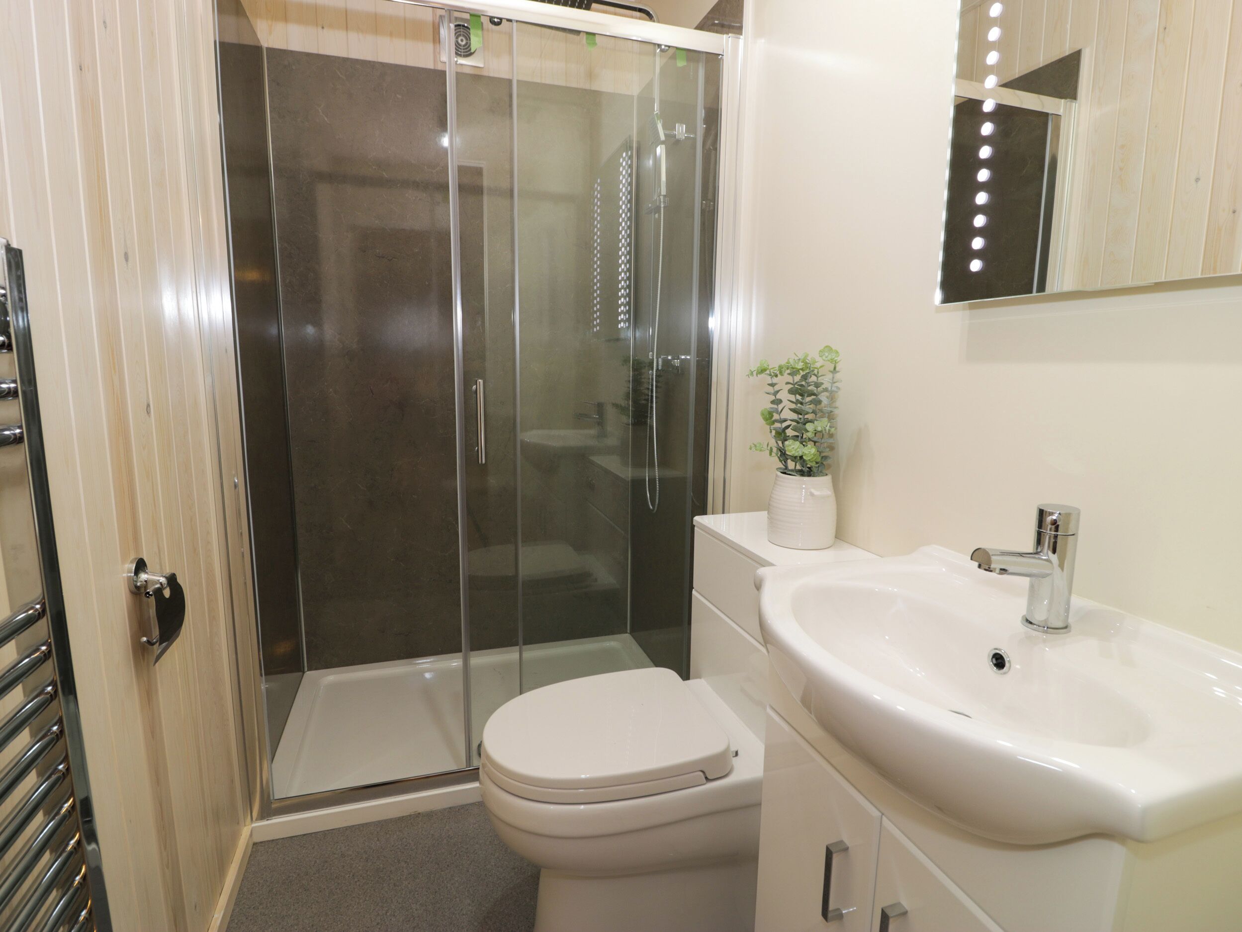 Un bagno moderno con doccia vetrata, un water bianco, un lavandino con specchio e una pianta in vaso sul mobile.
