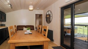 A dining area with a wooden table and chairs, a potted plant, and a view of the outdoors through a sliding door. - Betsi (Ruthin)