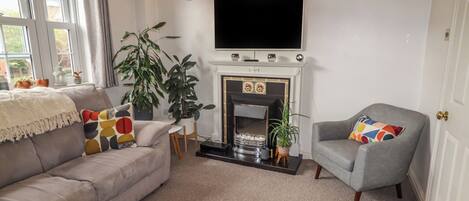 Una sala de estar con chimenea, un sofá, un sillón y un televisor.