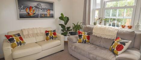 A living room with two sofas, a large painting, and a window with plants.