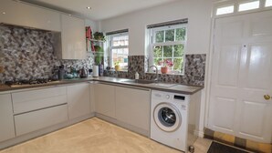 A modern kitchen with a built-in washing machine, a sink, and a window with a view of greenery. - 8 Nicholas Court (Chester)