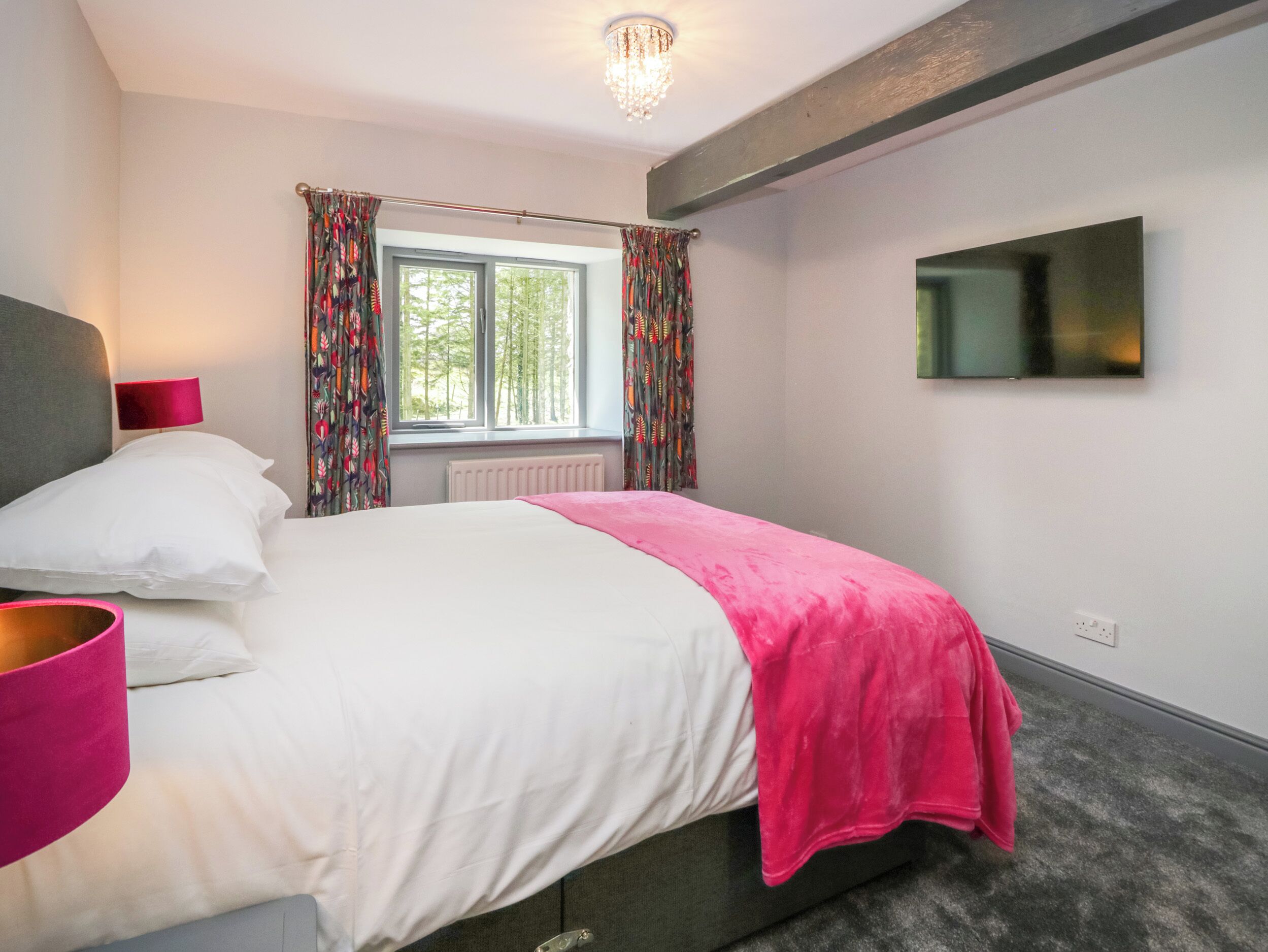 A bedroom with a bed, a TV mounted on the wall, and a window with curtains.