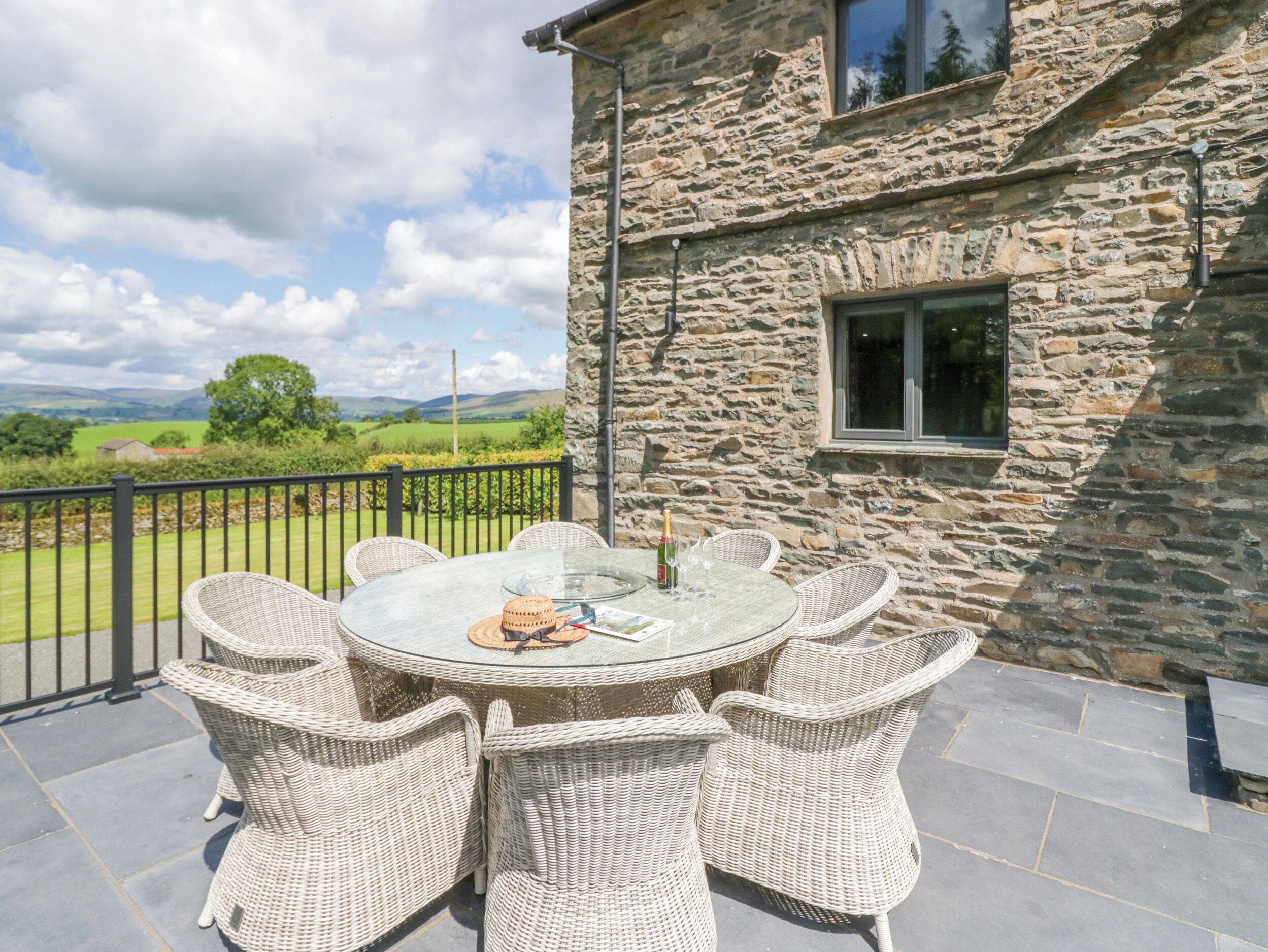 Un bâtiment en pierre avec une table ronde en verre et des chaises en osier sur une terrasse.
