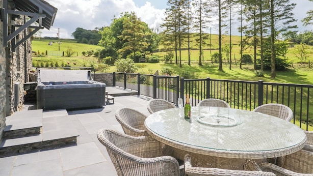 An outdoor patio with wicker furniture, a glass table, and a barbecue grill. - Fell View House (Kendal)