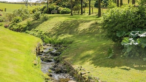 A lush green landscape with a small stream, trees, and a bench in the background. - Fell View House (Kendal)