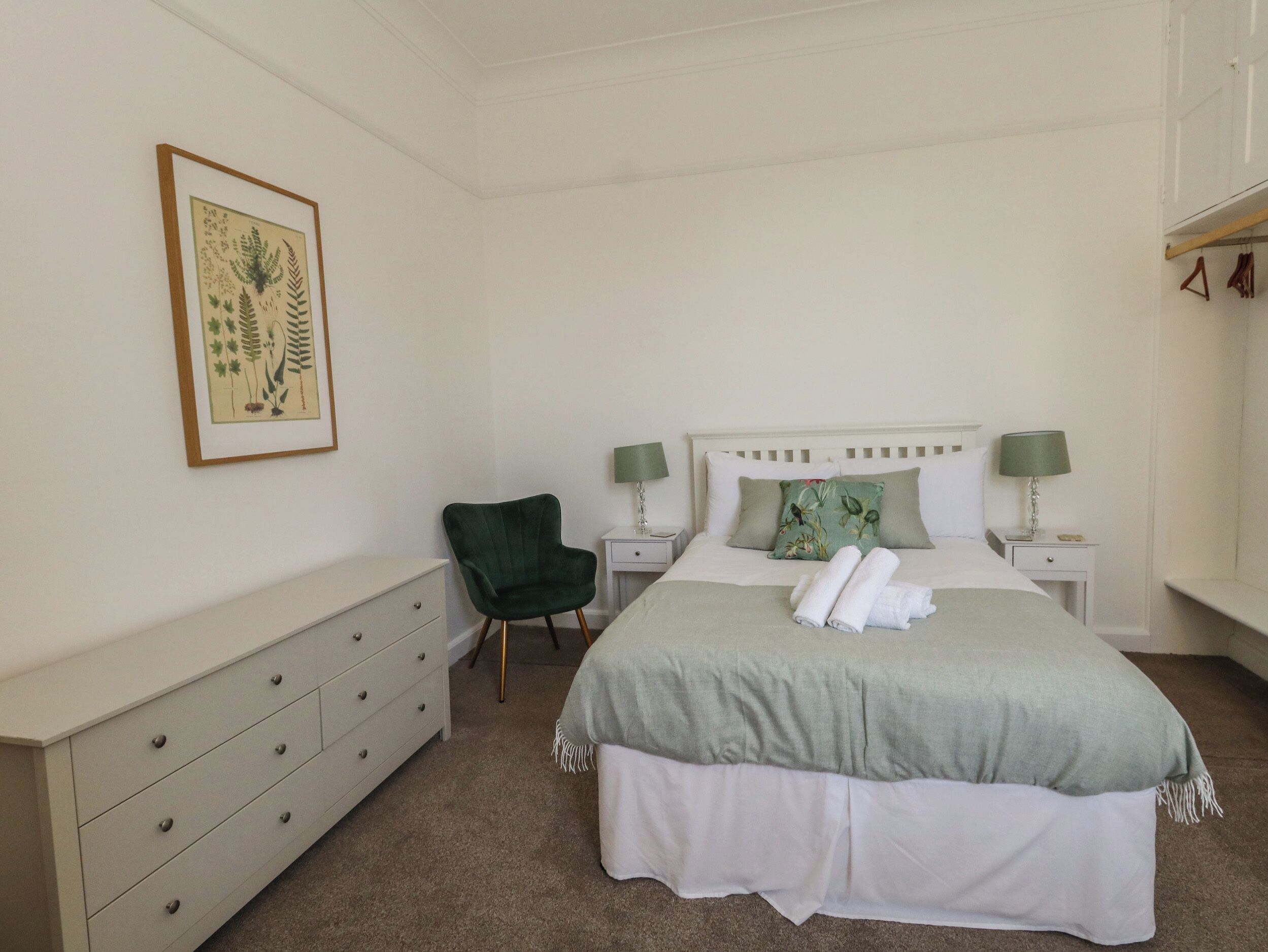 A bedroom with a bed, two bedside tables, a chair, a dresser, and a framed botanical print on the wall.
