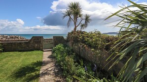 A pathway leading to a coastal area with a view of the sea, a palm tree, and a stone wall. - Blue Yonder (Weymouth)