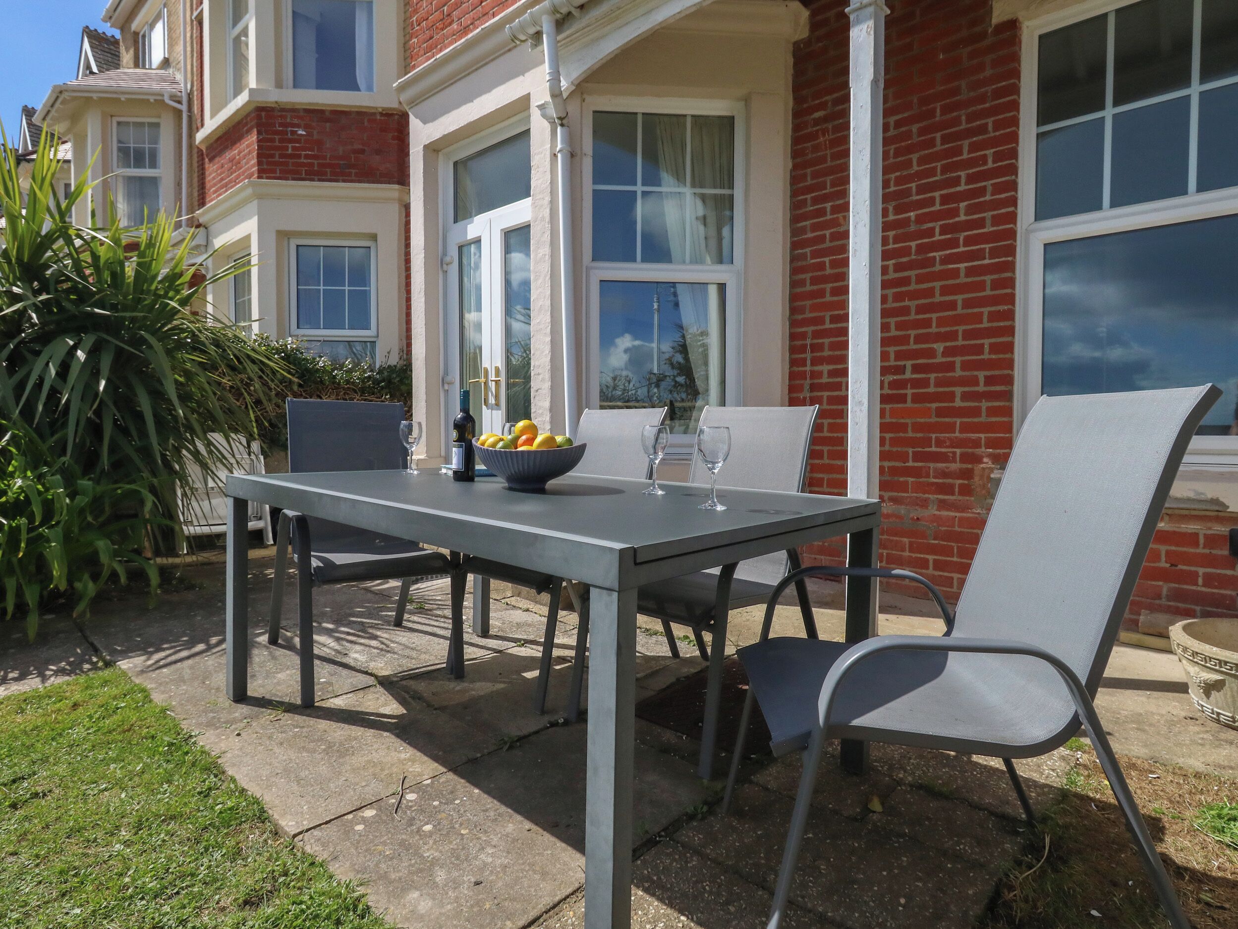 An outdoor patio with a table set for two, a bowl of fruit, and a bottle of wine.