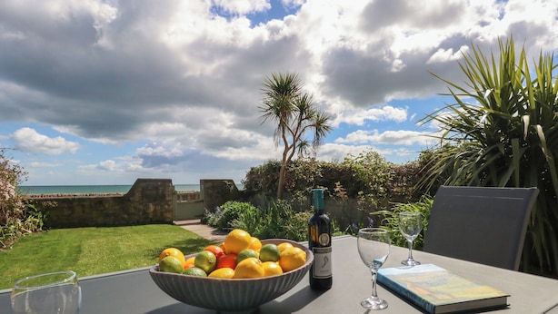 A table with a bowl of fruit, a bottle, and a book, overlooking a coastal view. - Blue Yonder (Weymouth)
