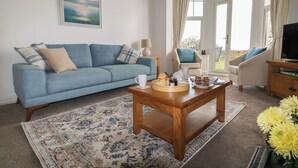 A living room with a blue sofa, a coffee table, a TV, and a window with curtains. - Blue Yonder (Weymouth)