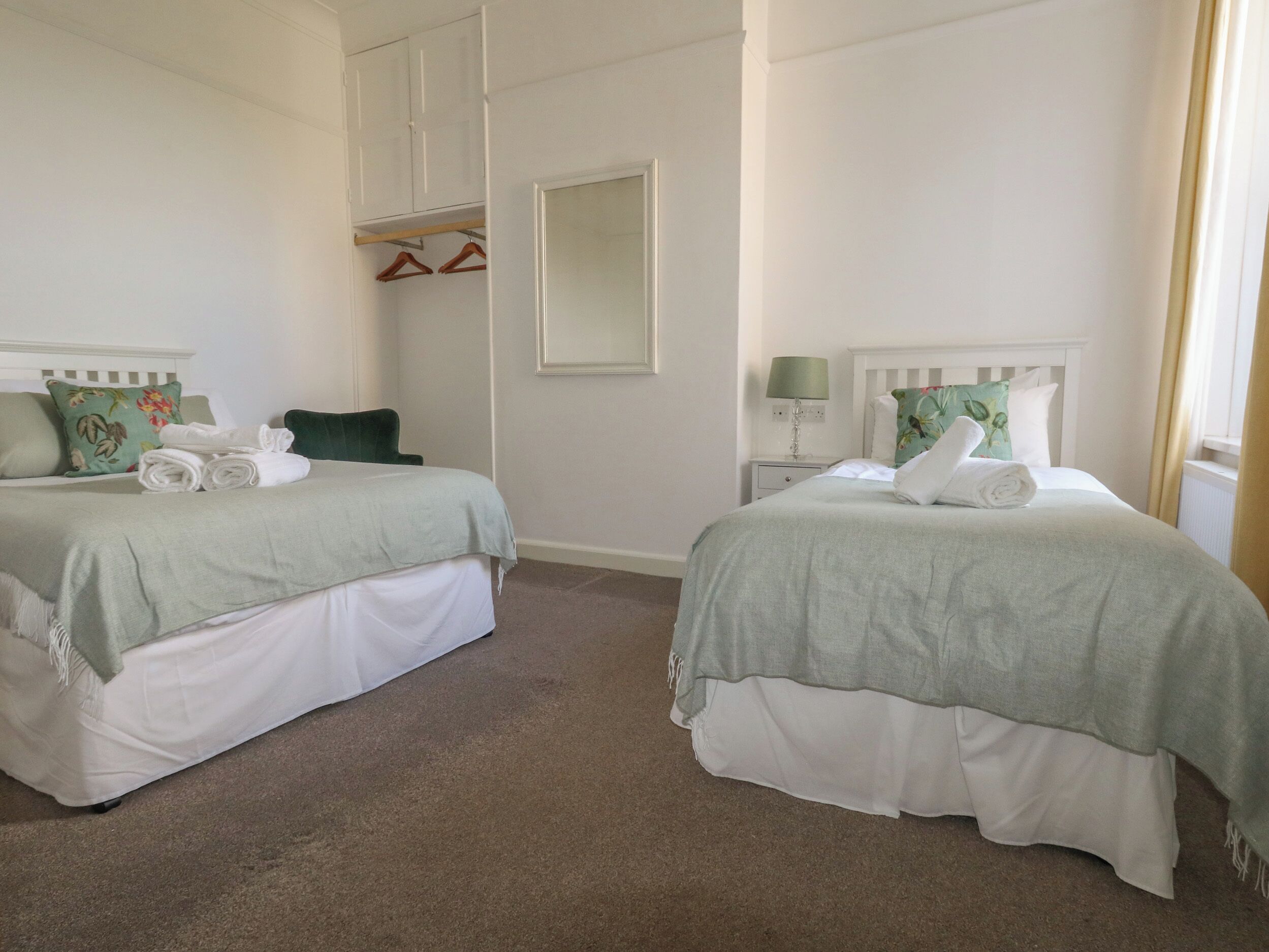 A hotel room with two beds, a closet, a mirror, and a nightstand with a lamp.