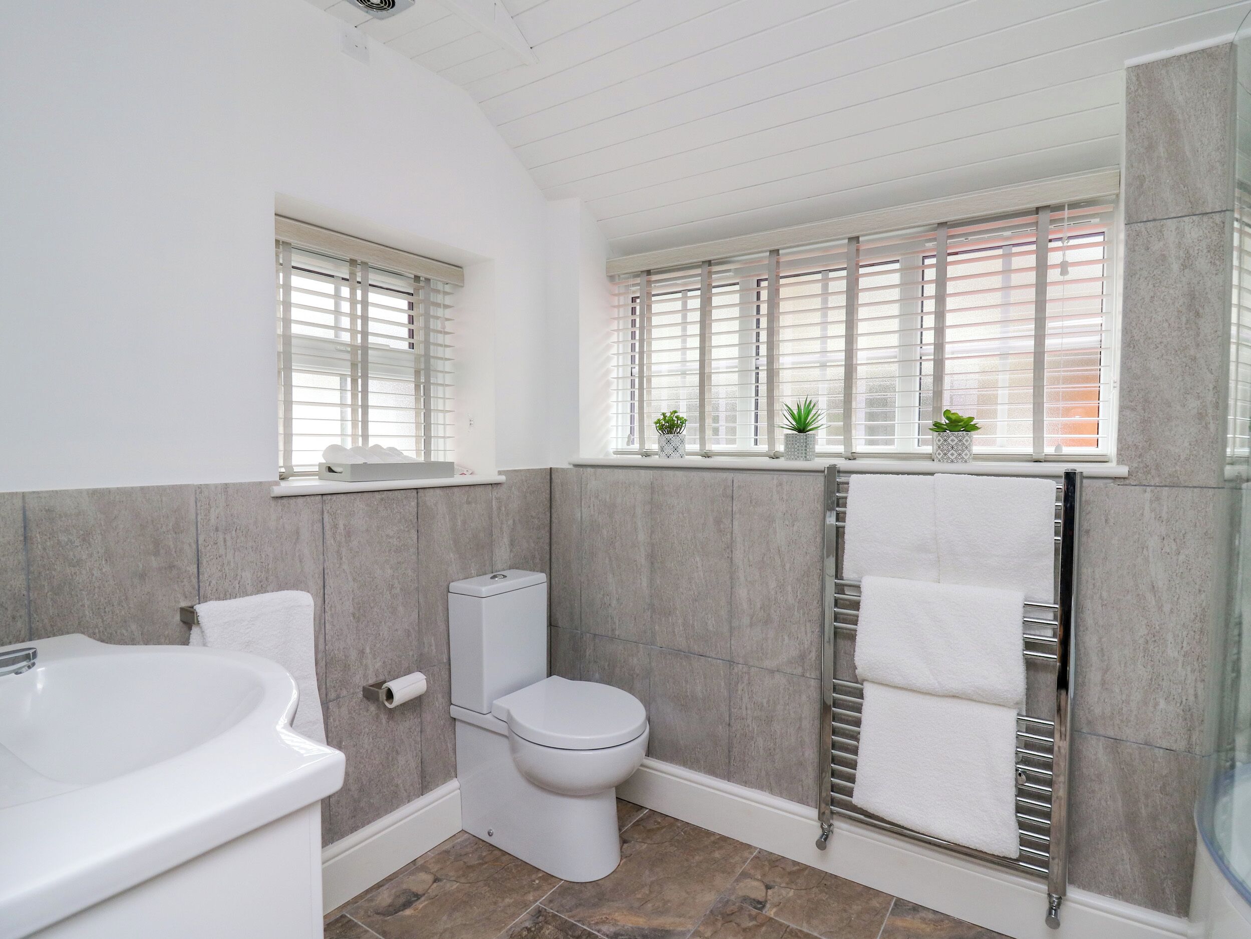 Un baño moderno con bañera, inodoro y ventana con persianas.
