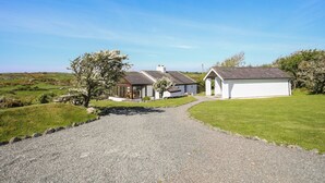 A gravel path leading to a white building with a sloped roof, surrounded by greenery and a clear blue sky. - Ty Mynydd (Holyhead)