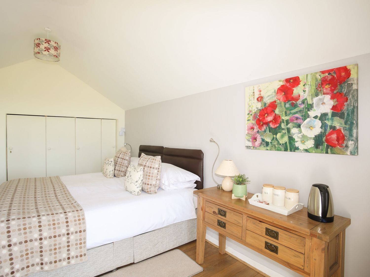 Een slaapkamer met een bed, kussens, een nachtkastje, een lamp, een schilderij en een kledingkast.