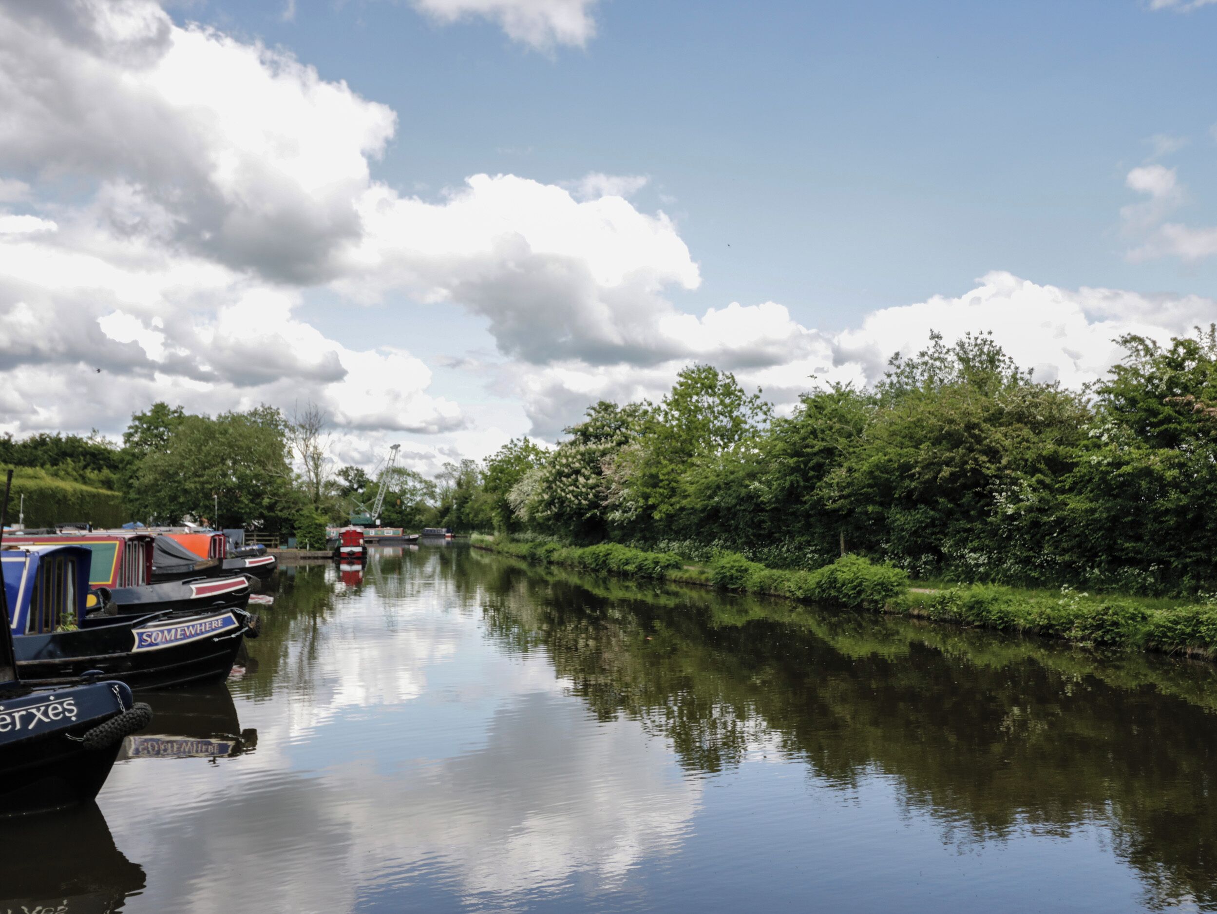 Ein ruhiger Fluss mit am linken Ufer vertäuten Booten, umgeben von üppigem Grün.
