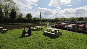 A riverside picnic area with benches and a boat docked on the river. - Above The Pub (Birmingham)