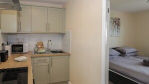 A compact kitchen with a microwave, sink, and stove, adjacent to a bedroom with a bed and a painting. - Above The Pub (Birmingham)
