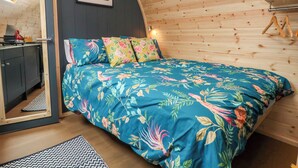 Un dormitorio acogedor con techo de madera curvada, ropa de cama floral, una pequeña zona de cocina y un cuadro enmarcado en la pared.