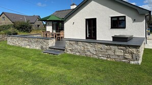 Una casa con base de piedra, un patio con mobiliario exterior y un cielo despejado.