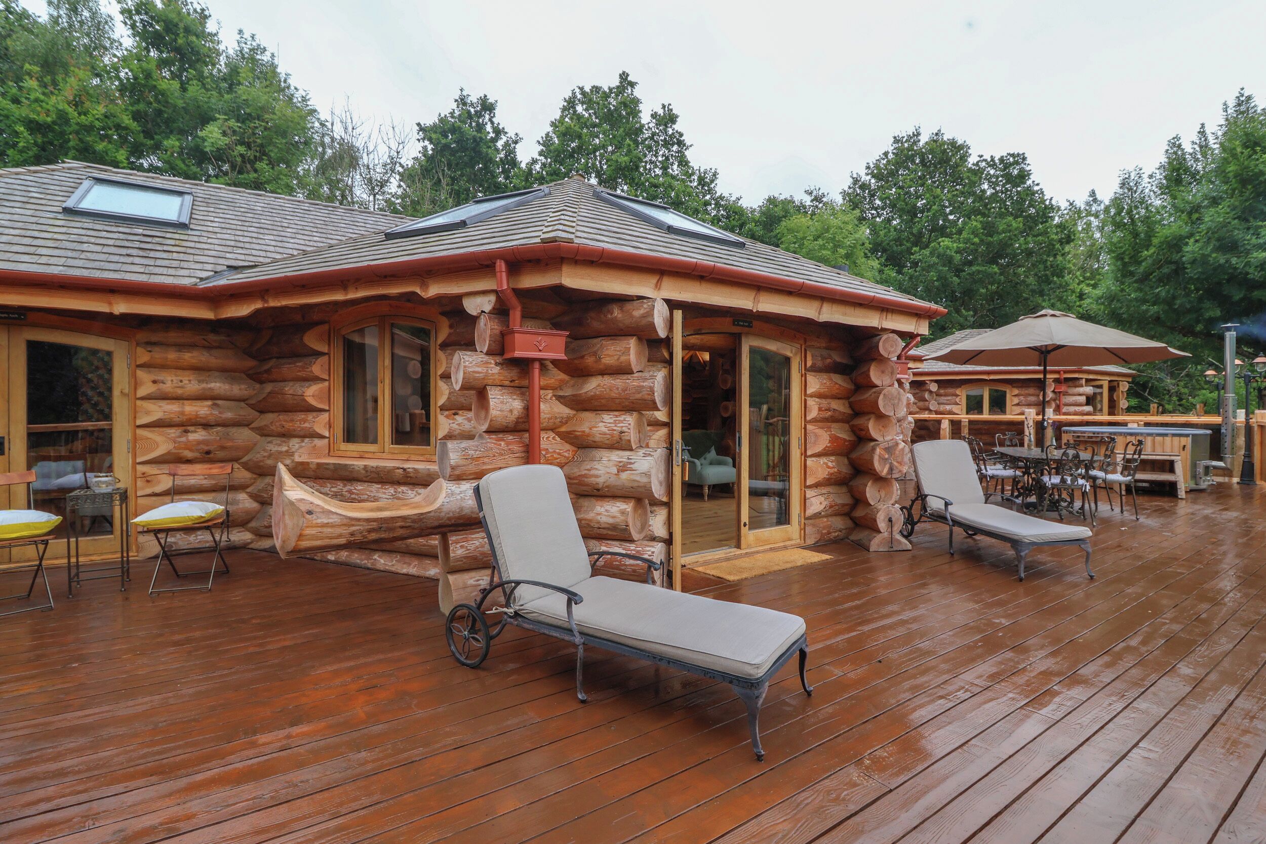 Eine Blockhütte mit einer Holzterrasse, zwei Liegestühlen und einem Tisch mit Stühlen.