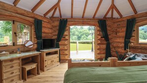 A log cabin room with a wooden desk, a bed, and a view of the outdoors. - Copper Lodge (Chulmleigh)