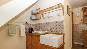 Une cuisine avec des meubles de rangement en bois, un évier blanc, une bouilloire et un égouttoir placé au-dessus du plan de travail.