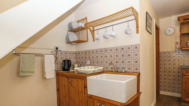 A kitchen with wooden cabinets, a white sink, a kettle, and a drying rack above the counter. - Country View (Caernarfon)