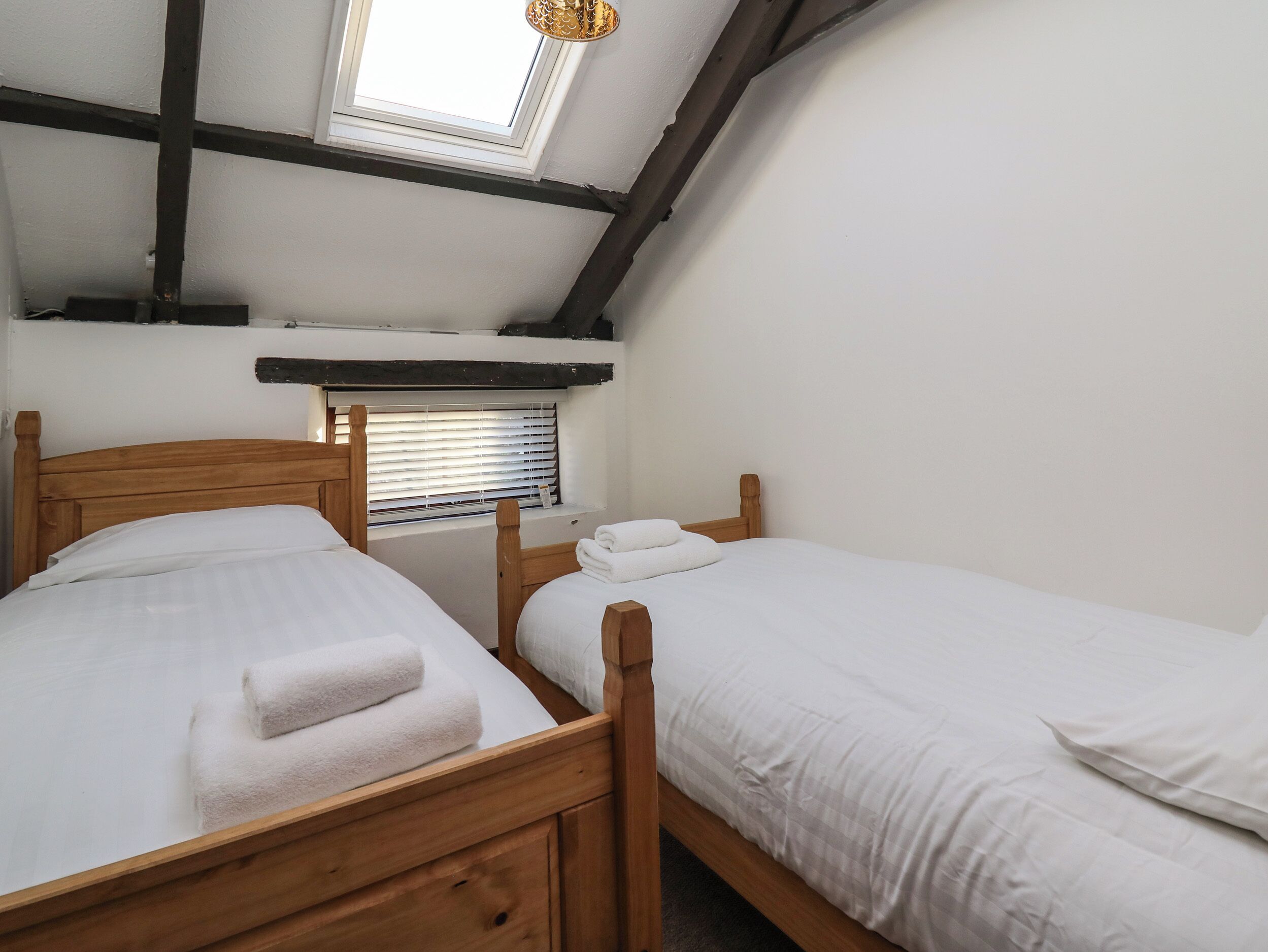 Une chambre à coucher avec deux lits en bois, un puits de lumière et une fenêtre avec des stores.