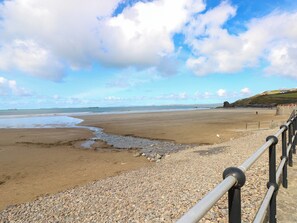 A beach with a pebble path, a railing, and a distant ship.