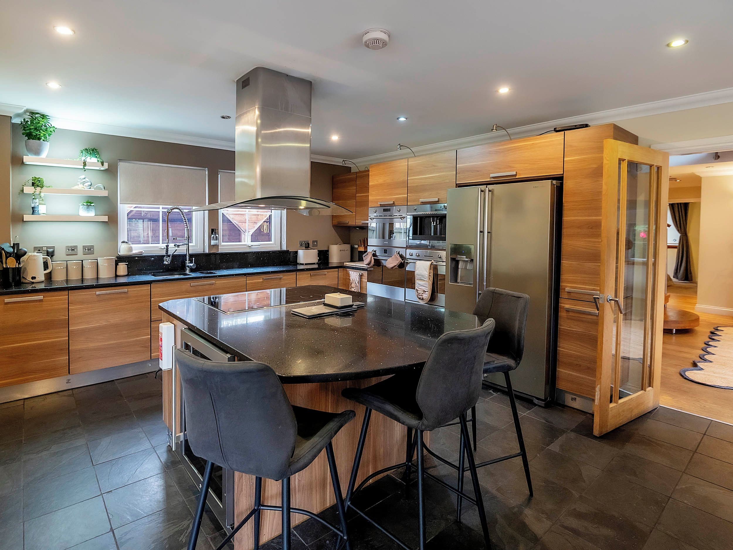 A modern kitchen with a central island, bar stools, stainless steel appliances, and wooden cabinetry.