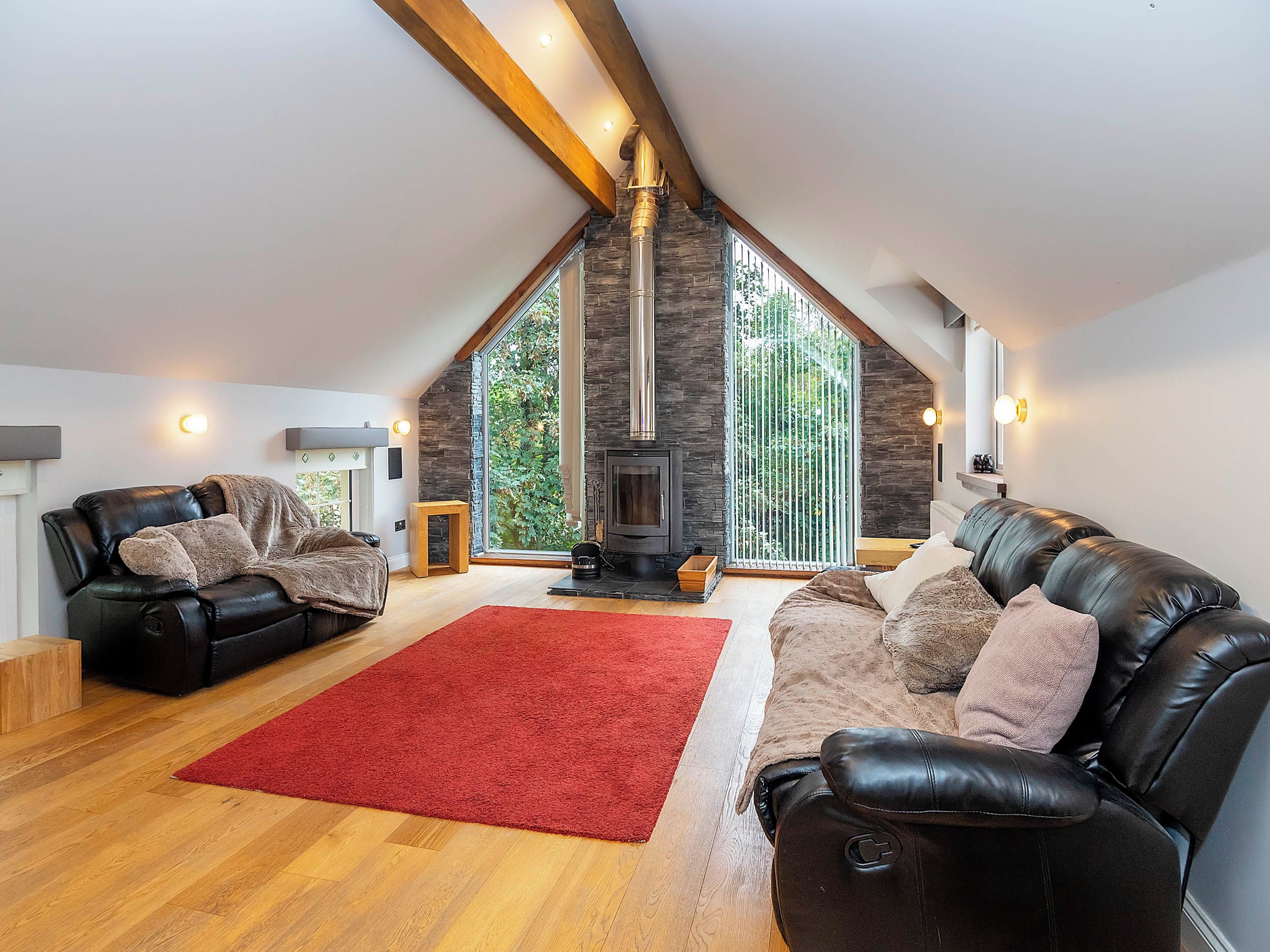 A spacious loft with a high ceiling, a stone fireplace, leather sofas, and a red rug.