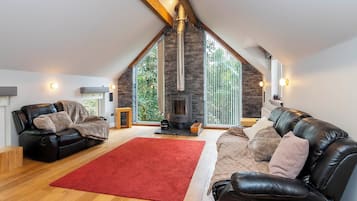 A spacious loft with a high ceiling, a stone fireplace, leather sofas, and a red rug.