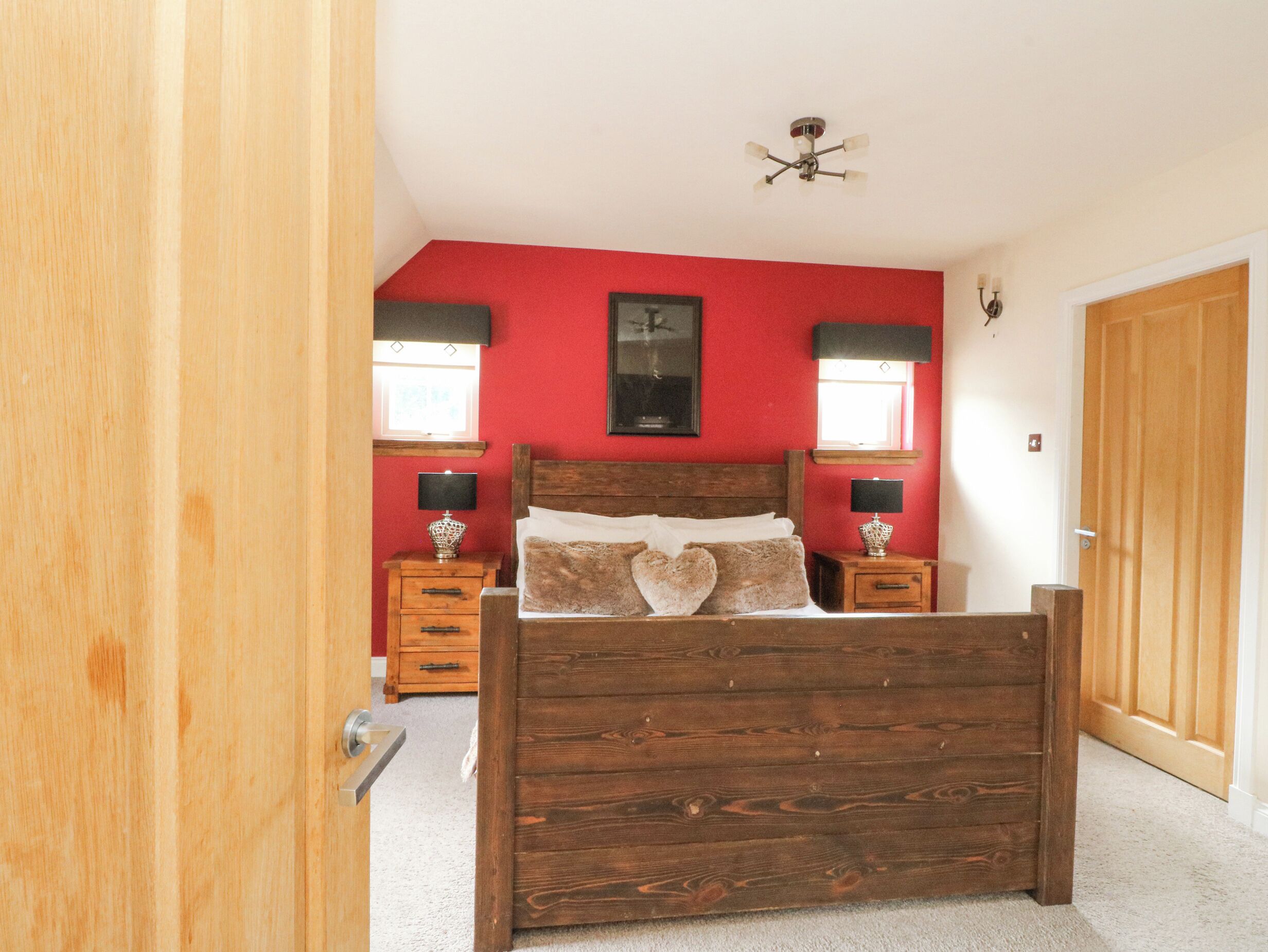 A bedroom with a wooden bed, red walls, two bedside tables with lamps, and a ceiling fan.