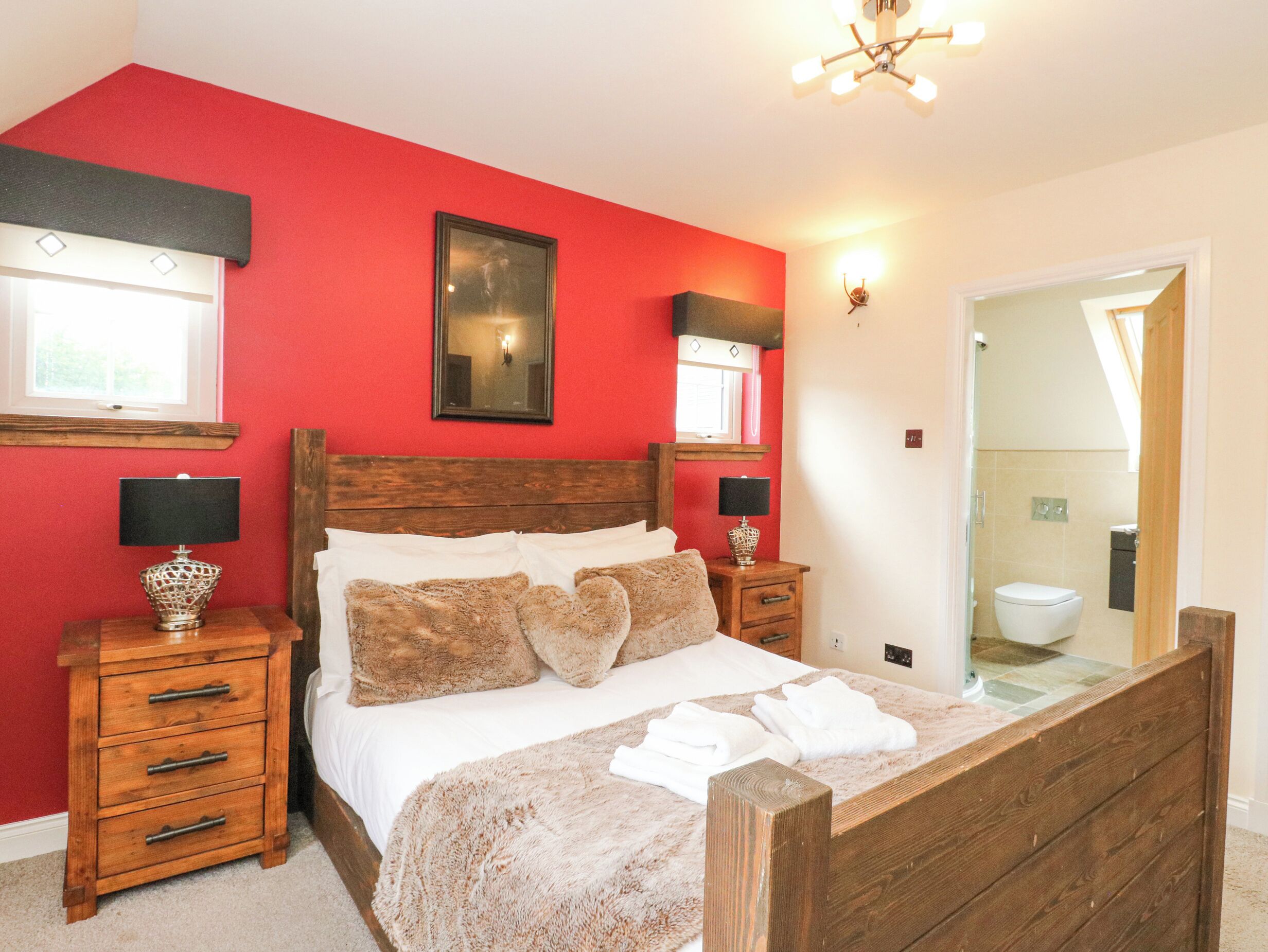 Een slaapkamer met een houten bed, rode wanden en een badkamer die zichtbaar is door een geopende deur.